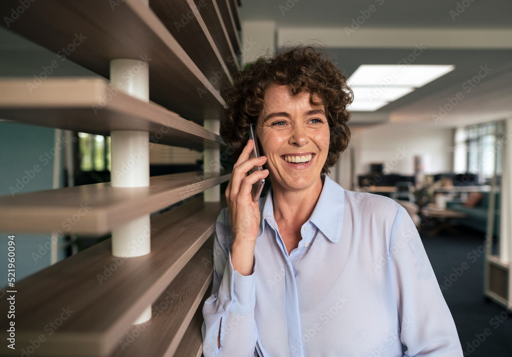 Cheerful businesswoman with curly hair talking on smart phone in office