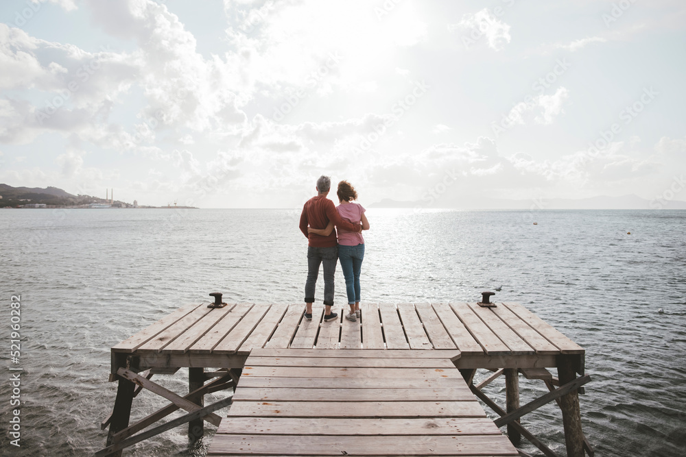 Mature couple standing on jetty under cloudy sky Mature couple standing on jetty under cloudy sky