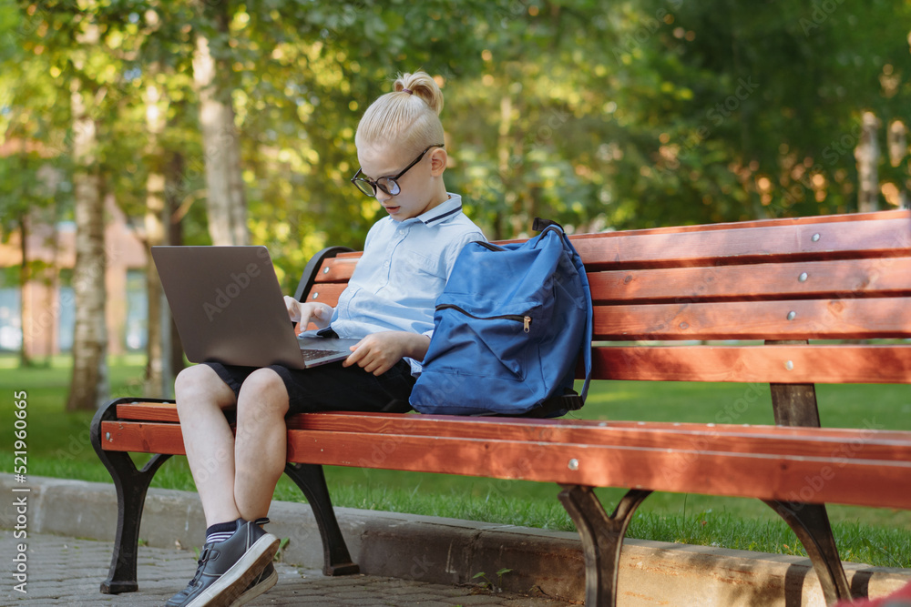 cute caucasian boy sitting on bench in park with laptop computer. Black screen