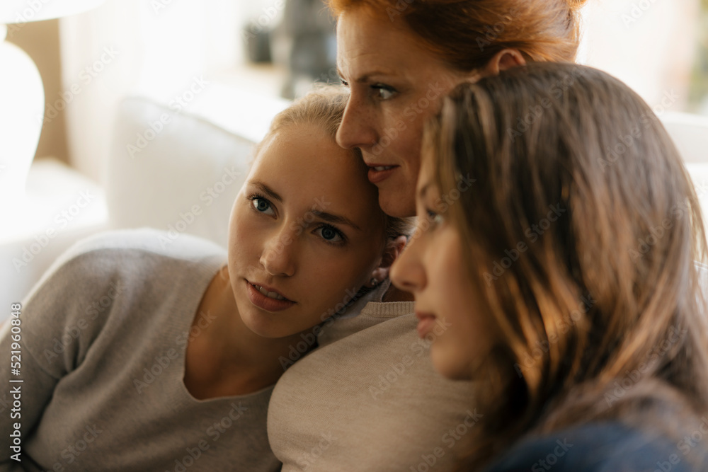 Affectionate mother with two teenage girls on couch at home Affectionate mother with two teenage girls on couch at home