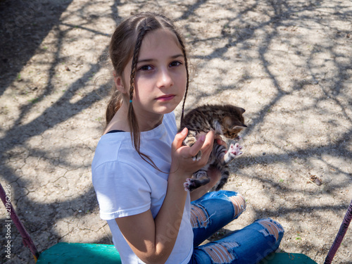 A teenage girl with a friendly face gently holds a striped kitten, looks at the camera