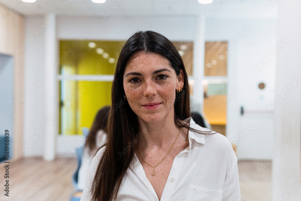 Portrait of confident businesswoman in office with colleagues in background Portrait of confident businesswoman in office with colleagues in background