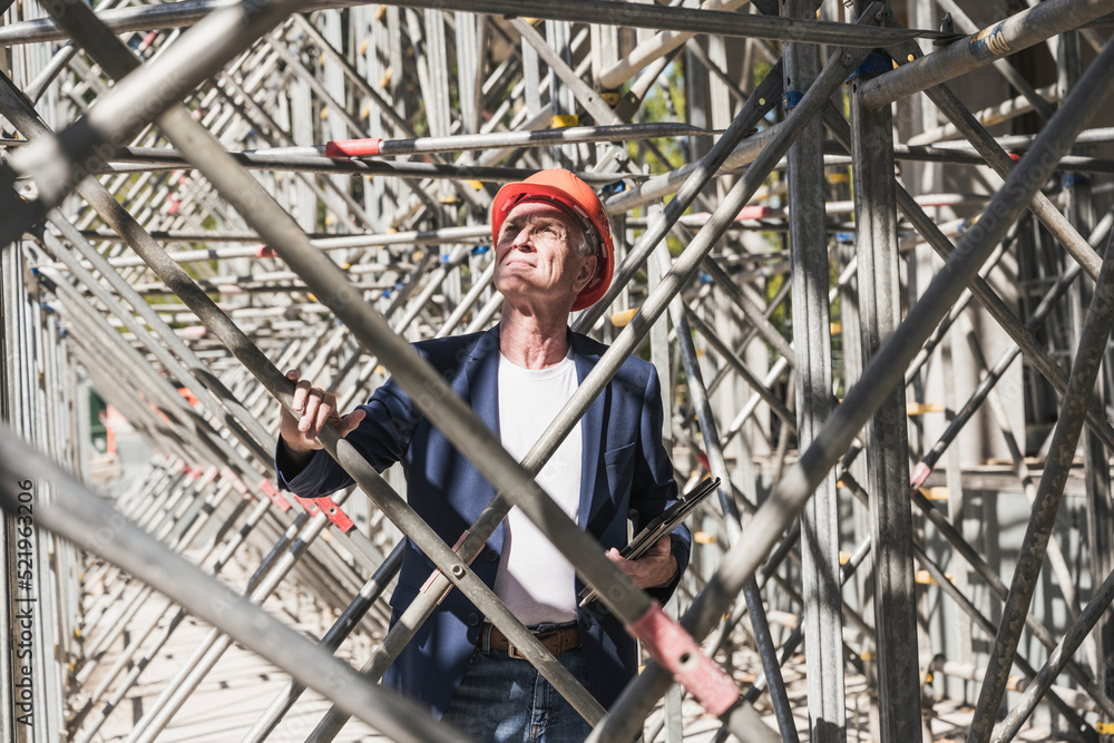 Engineer examining scaffolding at construction site on sunny day Engineer examining scaffolding at construction site on sunny day