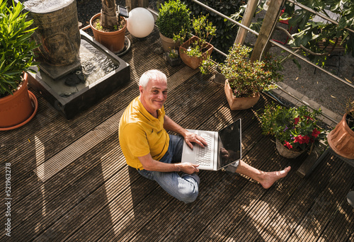 Smiling man with laptop sitting on terrace photo