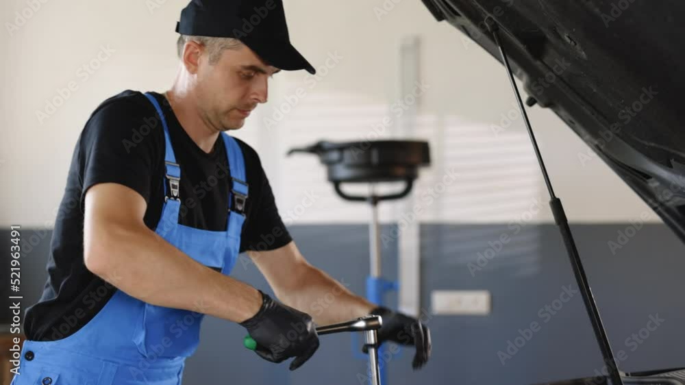 Portrait Empowering Male Car Mechanic is Working on a Vehicle in a Service Looks Happy While Using a Ratchet. Specialist is Looks at Camera and Smiles Portrait Empowering Male Car Mechanic is Working on a Vehicle in a Service Looks Happy While Using a Ratchet. Specialist is Looks at Camera and Smiles