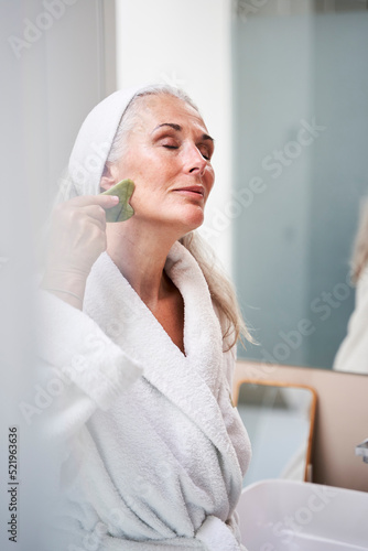 Beautiful woman massaging with jade stone in bathroom photo