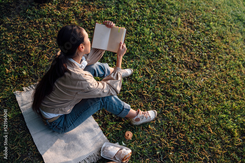 Woman reading book with food sitting on grass at park