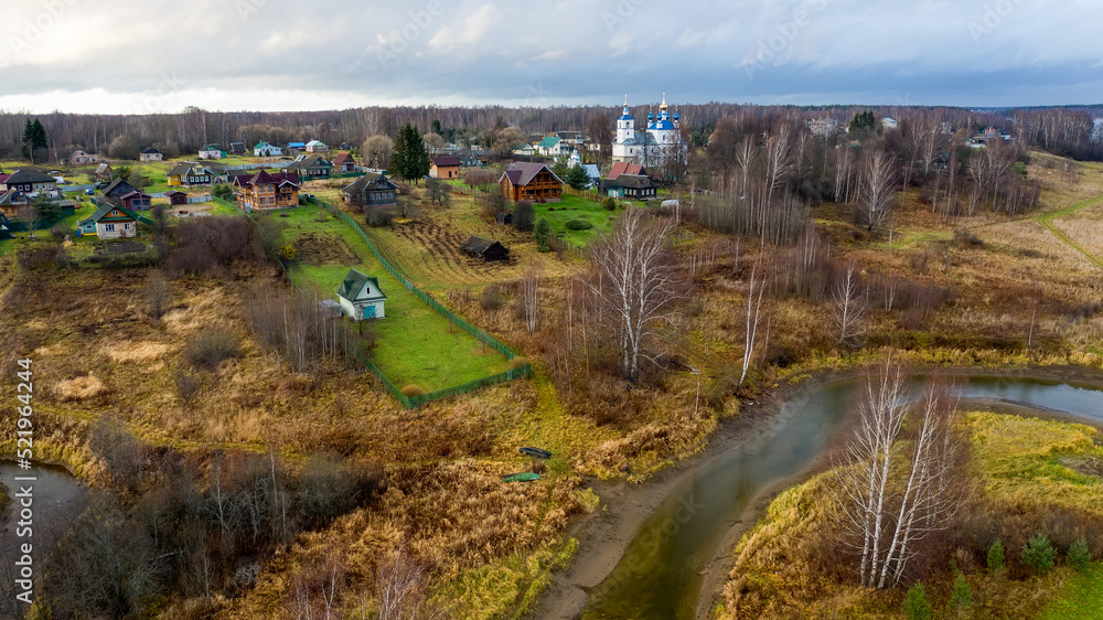 Aerial view of the village on a high hill above the river at sunrise in autumn. Aerial view. Residential buildings and a church, river bends, meadows, orange grass, trees at dawn.