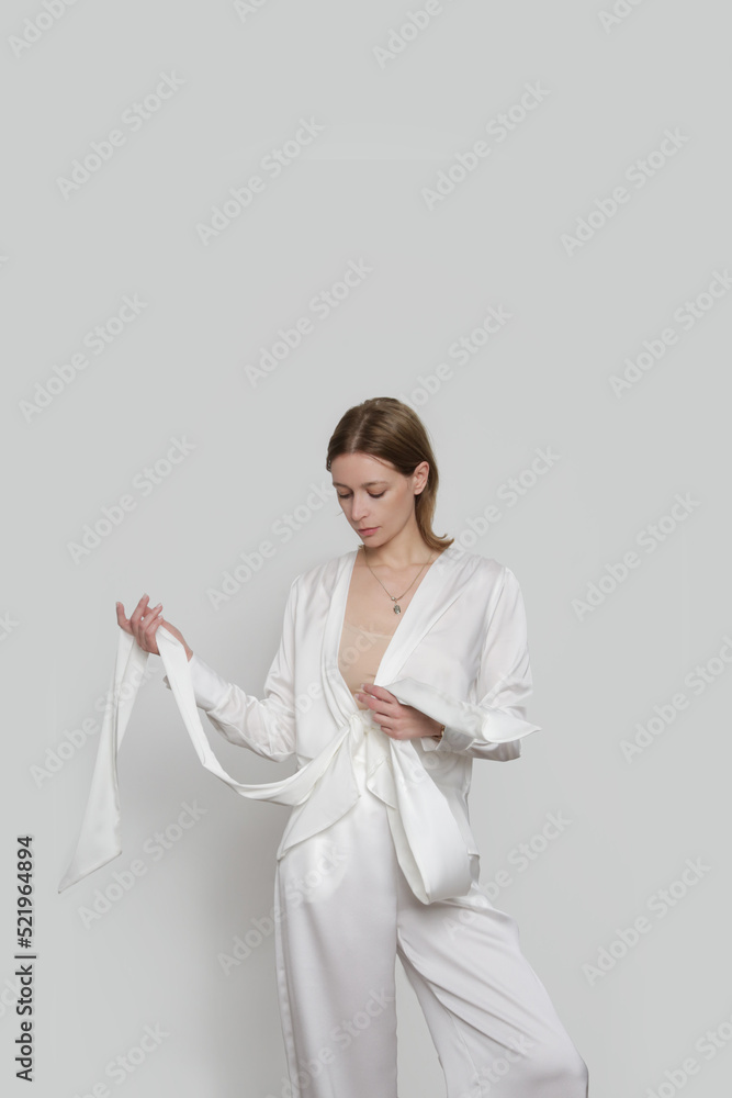 Serie of studio photos of young female model wearing all white classic outfit, silk satin wrap blouse and wide legged trousers. Serie of studio photos of young female model wearing all white classic outfit, silk satin wrap blouse and wide legged trousers.