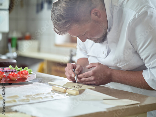Confectioner writing on marzipan with chocolate icing at kitchen photo