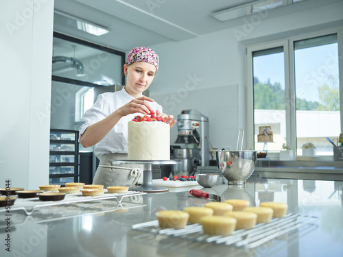 Young confectioner decorating cake with strawberries in kitchen photo