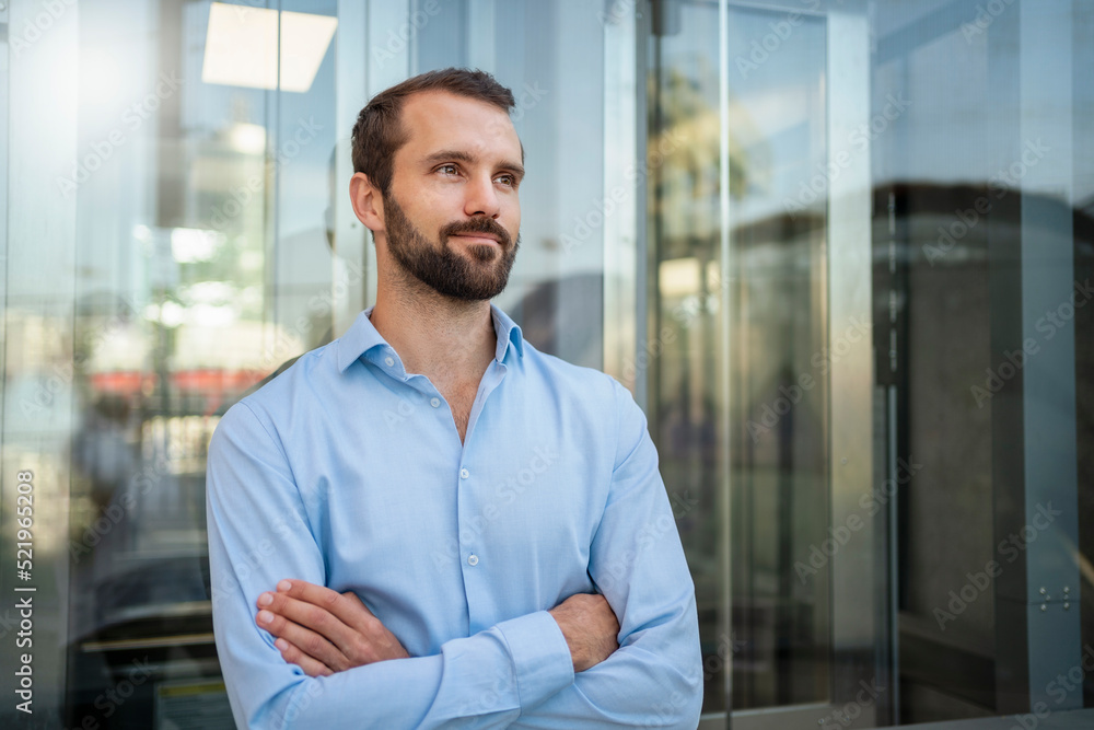 Smiling young businessman with arms crossed standing in front of glass Smiling young businessman with arms crossed standing in front of glass