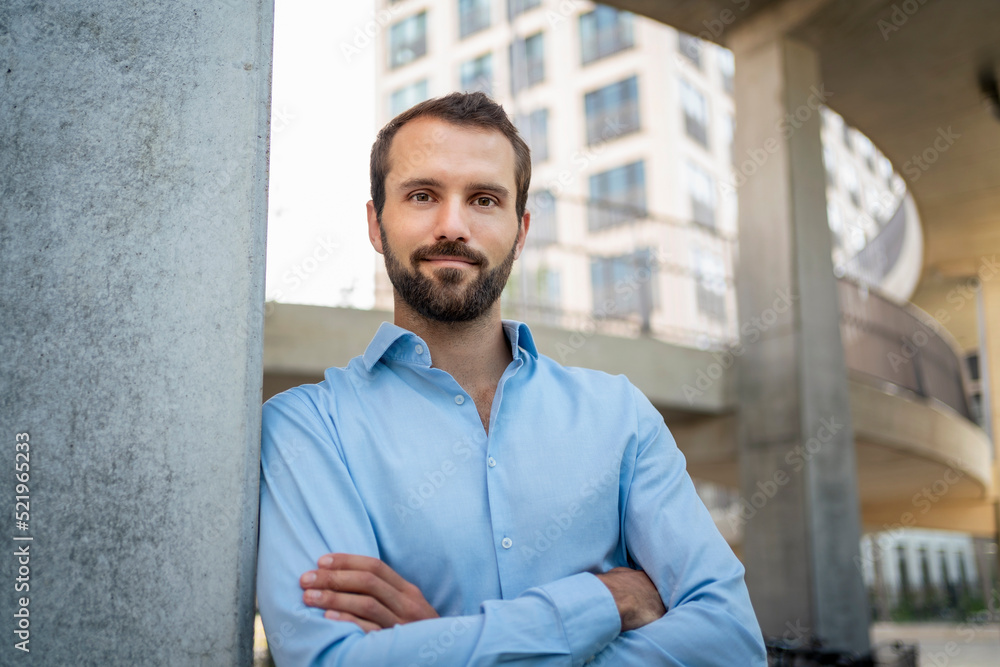 Smiling businessman with arms crossed leaning on wall in front of building Smiling businessman with arms crossed leaning on wall in front of building