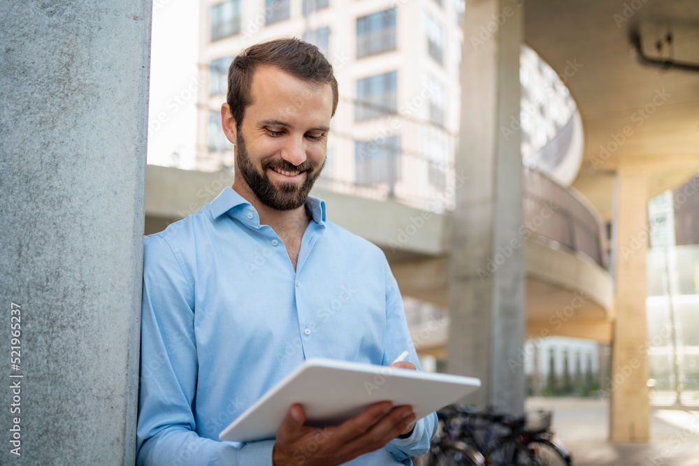 © Westend61 - Smiling young businessman using tablet PC standing under bridge