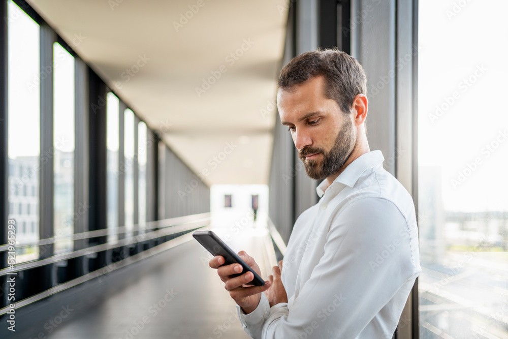 Young businessman using smart phone standing by window on elevated walkway Young businessman using smart phone standing by window on elevated walkway