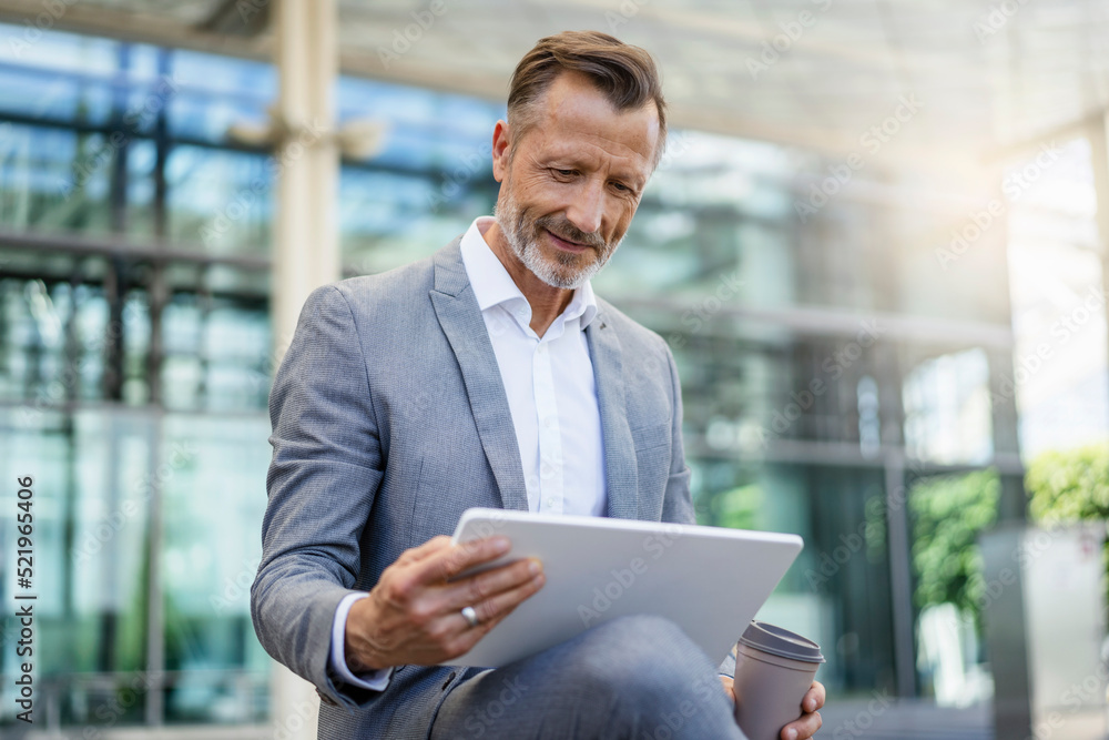 Smiling businessman holding reusable coffee cup using digital tablet Smiling businessman holding reusable coffee cup using digital tablet