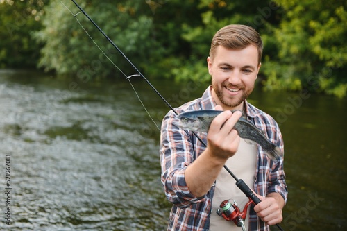 Happy fisherman holding a fish caught. Fishing on the beautiful river.