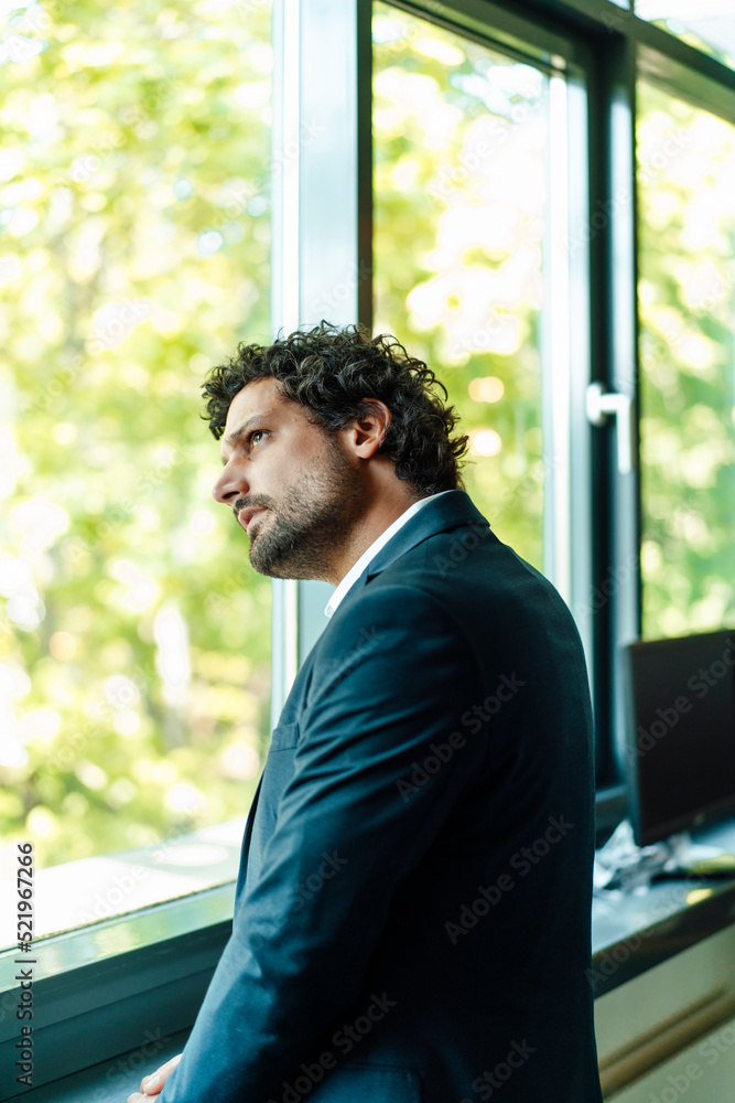 Contemplative businessman looking out through window at office Contemplative businessman looking out through window at office