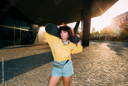 Young woman with skateboard standing under bridge at sunset photo