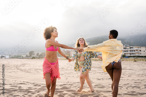 Multiracial women in swimwear playing ring around the rosy at beach photo