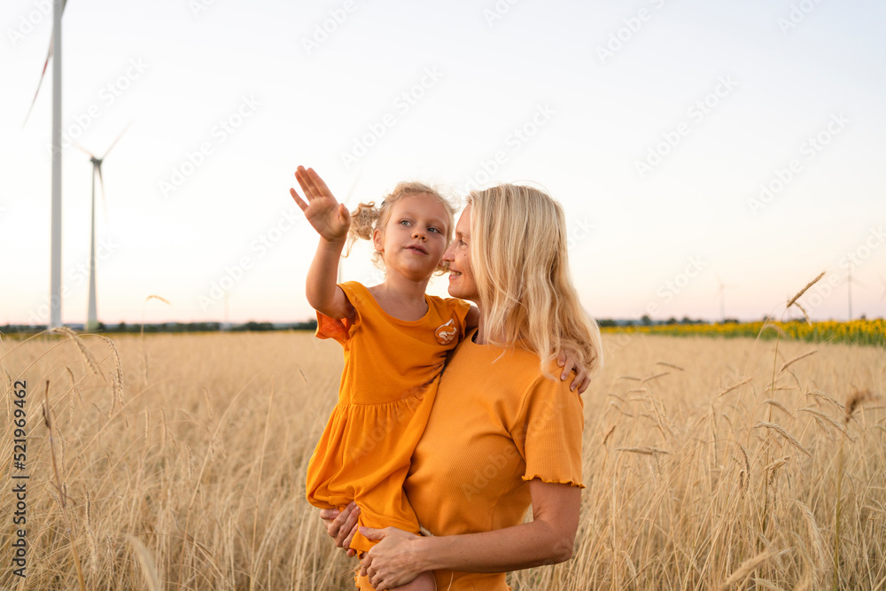 Smiling woman carrying daughter gesturing in wheat field Smiling woman carrying daughter gesturing in wheat field