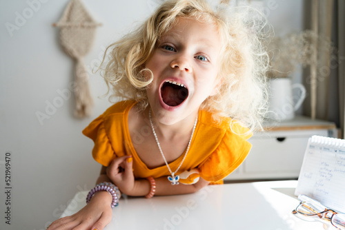 Blond girl with mouth open leaning on table at home photo