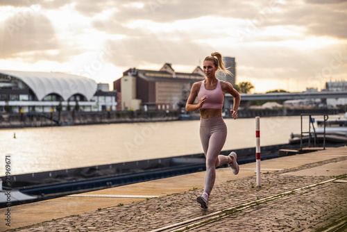 Blond woman jogging in front of river at sunset photo