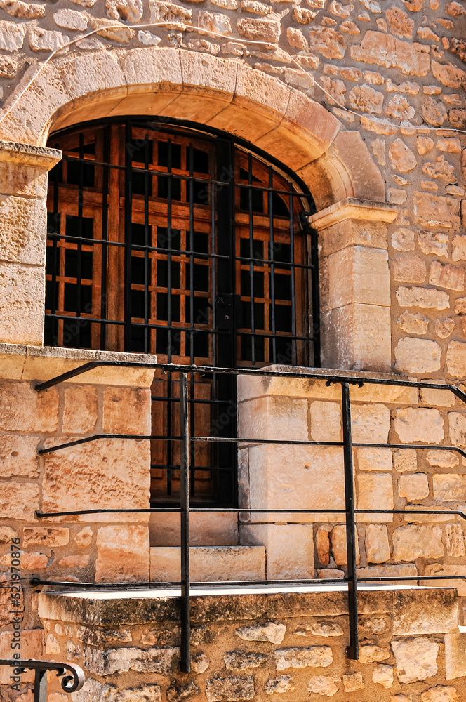 front view, medium distance of, a golden colored, stone wall with entrance door and stone, stairs, with black, iron, railings