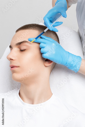 Men s cosmetology. Beautician makes a man a rejuvenation injection procedure of a handsome young man in a beauty salon.
