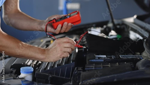 Professional car mechanic check battery voltage with electric multimeter. Automobile diagnosis. Car mechanic repairer looks for engine failure on diagnostics equipment in vehicle service workshop