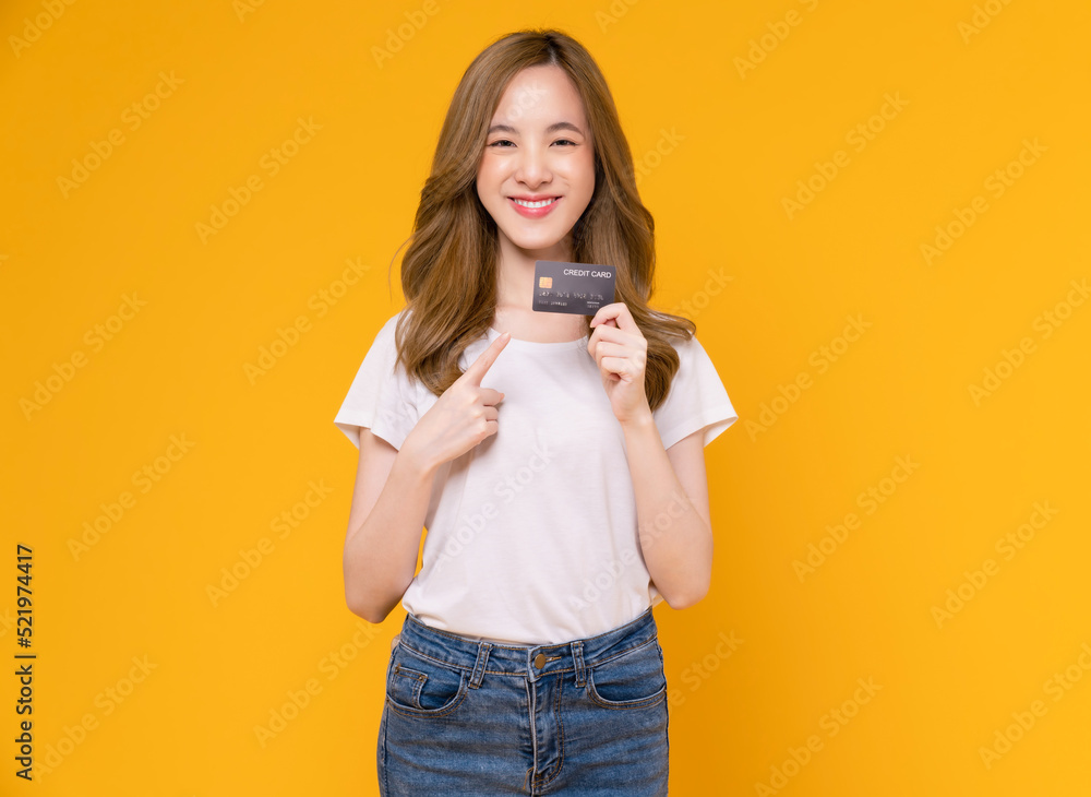 Cheerful beautiful Asian woman in white t-shirt and holding mockup credit card on yellow background. Cheerful beautiful Asian woman in white t-shirt and holding mockup credit card on yellow background.