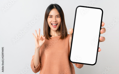 Beautiful Asian woman holding smartphone mockup of blank screen and shows ok sign on grey background