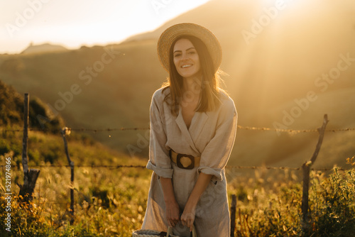 Portrait of a happy woman walking with a straw bag through the field at sunset