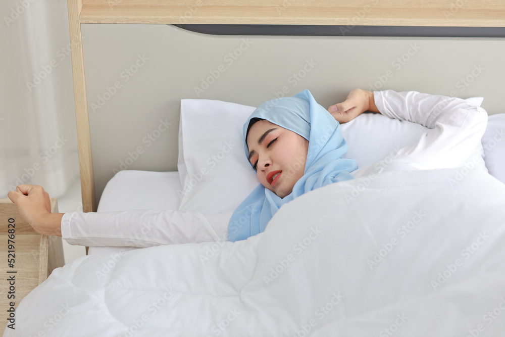 Beautiful asian woman wearing white muslim sleepwear lying on bed, stretching her arms after getting up in the morning at sunrise. Cute young girl with hijab wake up and relaxing, closing her eyes Beautiful asian woman wearing white muslim sleepwear lying on bed, stretching her arms after getting up in the morning at sunrise. Cute young girl with hijab wake up and relaxing, closing her eyes