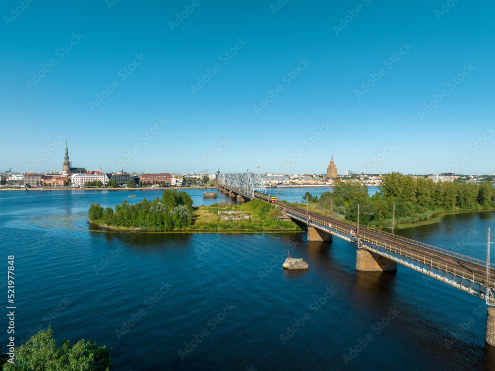 A bridge over river Daugava in Riga with a train passing by. Bridges in Latvia. Aerial Riga view.