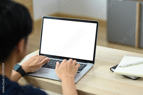 Over shoulder view of male freelancer sitting in bright living room and working online, searching information online on laptop computer