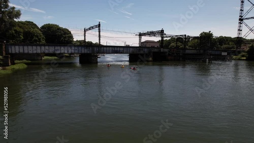 A low angle view of the Saugatuck River in Connecticut on a beautiful day. The drone camera dolly in towards a railroad bridge with three people paddling their kayaks under the bridge. photo