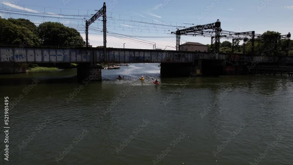 A low angle view of the Saugatuck River in Connecticut on a beautiful day. The camera dolly in towards a railroad bridge with three people paddling their kayaks under the rusty bridge. A low angle view of the Saugatuck River in Connecticut on a beautiful day. The camera dolly in towards a railroad bridge with three people paddling their kayaks under the rusty bridge.