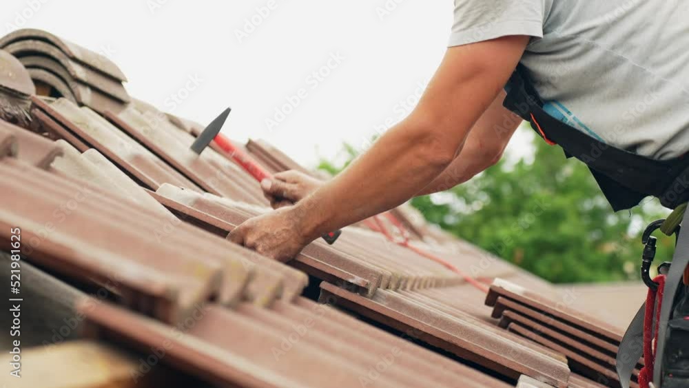 Roof worker using hammer and nails to put tiles into place, side view Roof worker using hammer and nails to put tiles into place, side view