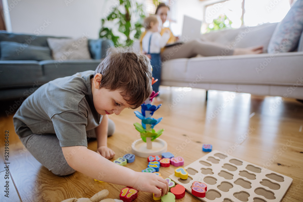 Little boy playing with montessori wooden toys in living room,mother and sister in backgroud. Little boy playing with montessori wooden toys in living room,mother and sister in backgroud.