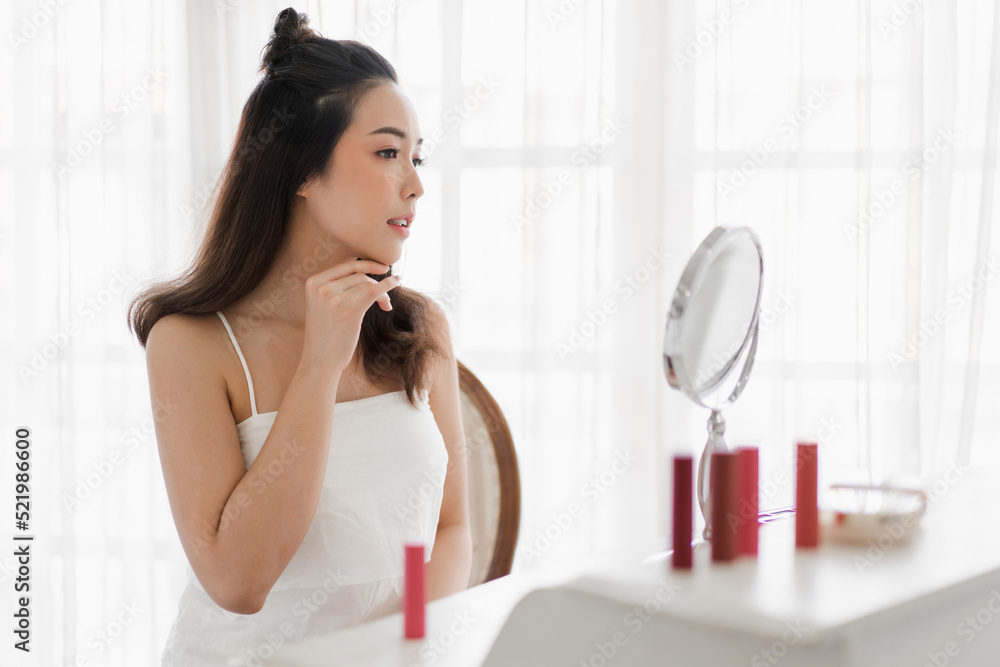 Smiling of young beautiful pretty asian woman clean fresh healthy white skin looking at mirror.asian girl touching on her face with hand and applying cream at home.spa and beauty concept Smiling of young beautiful pretty asian woman clean fresh healthy white skin looking at mirror.asian girl touching on her face with hand and applying cream at home.spa and beauty concept