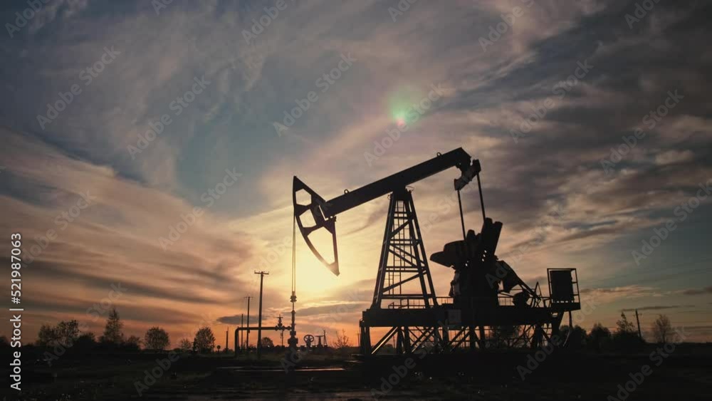 Low angle shot of silhouette of working oil pump from oil field at sunset. The industrial equipment. Oil industry, crude oil prices concept. Low angle shot of silhouette of working oil pump from oil field at sunset. The industrial equipment. Oil industry, crude oil prices concept.