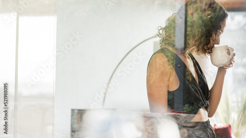 Woman drinking coffee in kitchen seen through window