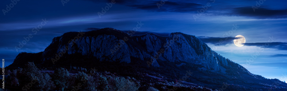 rocky formation in mountains at night. gorgeous autumn landscape in full moon light. trees on the hills in colorful foliage. mysterious atmosphere. halloween background