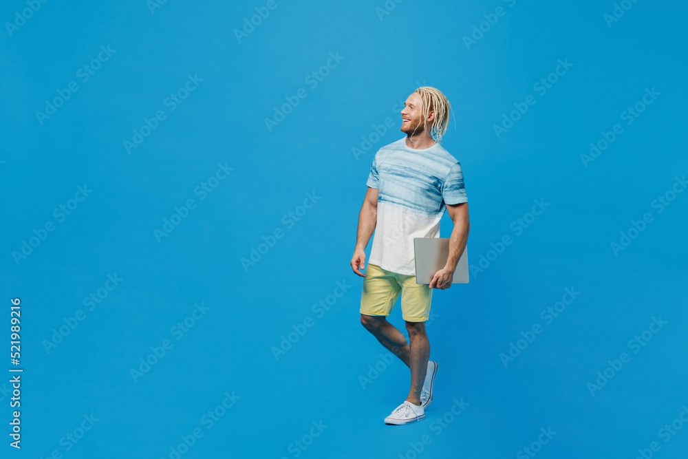 Full body young blond man with dreadlocks 20s he wear white t-shirt hold in hand closed laptop pc computer look aside on workspace area isolated on plain pastel light blue background studio portrait Full body young blond man with dreadlocks 20s he wear white t-shirt hold in hand closed laptop pc computer look aside on workspace area isolated on plain pastel light blue background studio portrait