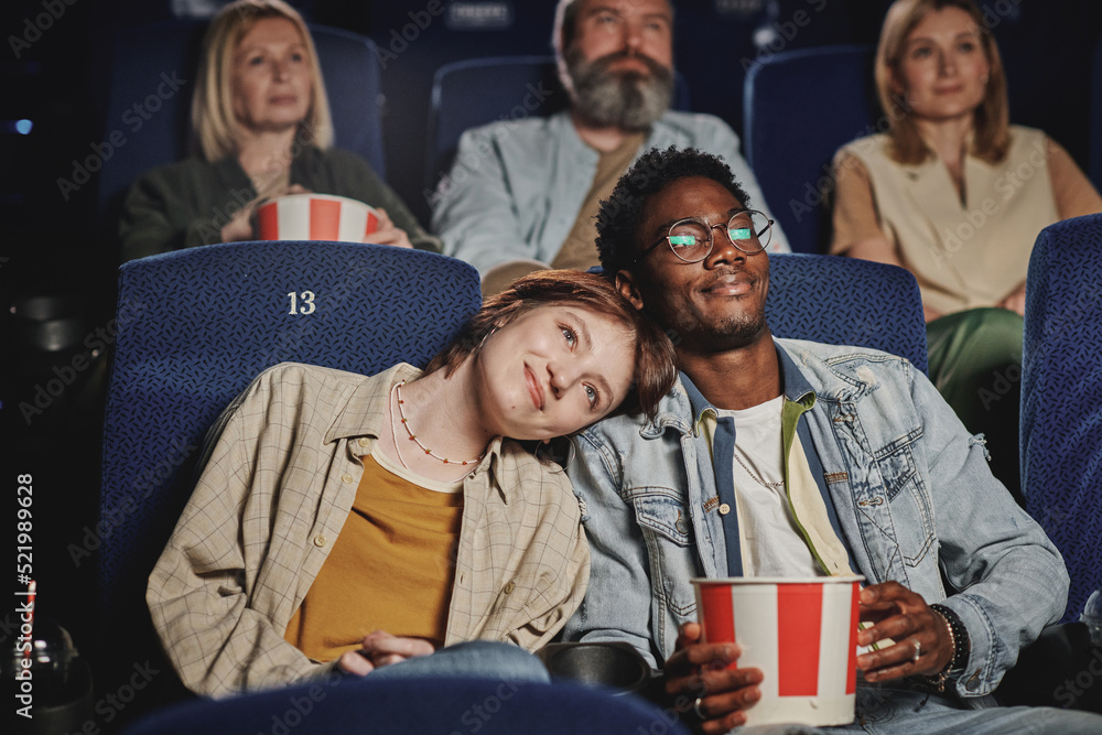 Portrait of modern lovey-dovey ethnically diverse young couple spending evening on date at cinema - obrazy, fototapety, plakaty 