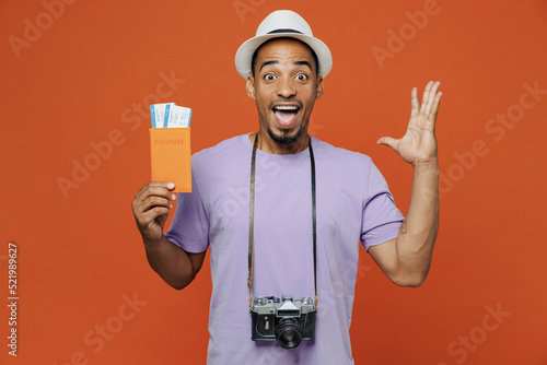 Traveler black man wear purple t-shirt hat hold pasport ticket spread hand isolated on plain orange color background. Tourist travel abroad in spare time rest getaway. Air flight trip journey concept.