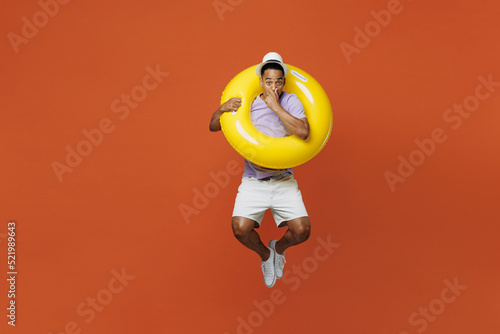 Full body traveler black man wear t-shirt hat rubber ring jump hold breathe isolated on plain orange color background Tourist travel abroad in spare time rest getaway. Air flight trip journey concept #521989643