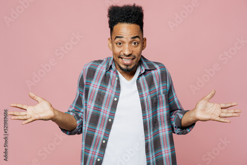 Tableau sur toile Young puzzled man of African American ethnicity wear blue shirt spread hands shrugging shoulders have no idea, stand questioned unaware I don't know why isolated on plain pastel light pink background