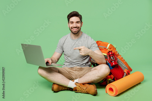Full size young traveler white man near backpack mat sit use work point on laptop pc computer isolated on plain green background. Tourist leads active lifestyle. Hiking trek rest travel trip concept. #521989887